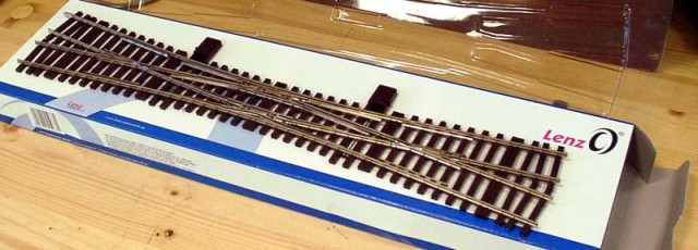 LENZ commercialise aussi une voie et ses divers éléments. Voici la TJD manuelle, le modèle motorisé et digitalisé est en fabrication. Le rail issu de la production Atlas correspond à un rail lourd (profil 3,75 mm ou code 148). Les traverses bien gravées reproduisent bien un travelage continental (ni britannique, ni américain) mais sont très (trop ?) régulières. Les attaches des rails sont assez discrètes et pas trop typées. Il est prévu la réalimentation des pointes de cœur. Les modélistes  sauront atténuer le clinquant et la régularité toute industrielle du modèle.<br />Voir le site LENZ "0". Déviation 12,5°. Rayon 1649,39mm (on pourra dire 1650!). Longueur de chaque partie droite 585,88mm.