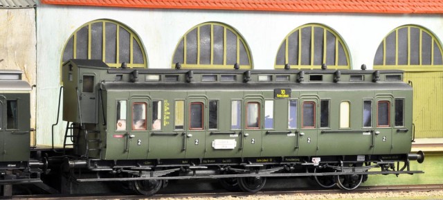 Menne - Voiture prussienne B3pr11en version DRG de 2ème classe (années 30)<br />Le modèle présenté, une B3pr11 à vigie, est un modèle unique (kitbashing) réalisé à partir d’éléments de voitures de 3ème classe Menne. La fabrication Menne (EM+EL) est une fabrication artisanale en plastique injecté qui remonte au début des années 80. Elle s’est (comme Lenz) d’abord attachée à reproduire la gamme complète des voitures métallisées DB (3 essieux et bogies) avant d’offrir certaines voitures prussiennes dont elles découlaient.  Ainsi les boites d’essieux sont des boites à rouleaux ! A noter que les voitures métallisées DB pouvaient être acquises en kit alors que les voitures prussiennes étaient livrées montées à partir d’éléments modulaires (selon une méthode proche des voitures britanniques de Ian Kirk).