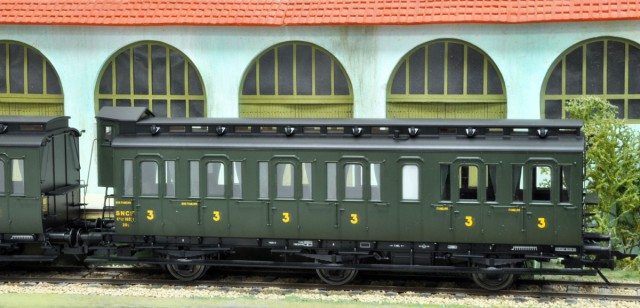 Après la voiture prussienne B3 Pr 10a présentée en version DB post 1956 à la dernière réunion, voici la voiture prussienne C3 Pr 11 avec guérite (en version SNCF) qui représente l’archétype de cette grande série de voitures à portières latérales lancée dans la 2ème décennie du siècle précédent. Ce sont donc des voitures récentes qui sont reçues en grand nombre (environ 700 exemplaires ?) en 1919 au titre de l’Armistice, ces voitures prussiennes 3 essieux  à portières latérales rouleront sur tous les réseaux avant d’être regroupées sur les Régions Nord et Est de la SNCF où elles achèvent leur carrière commerciale en 1962 ! La C3 pr 11 est équipée  de l’éclairage électrique et  son lanterneau n’a pas été tôlé. Si la plupart des voitures SNCF et DB eurent leur lanterneau tôlé dans la période d’après-guerre avec un seul aérateur conservé au niveau des toilettes, il existe des photos de voitures ayant conservé toutes les baies vitrées et les aérateurs sur leur lanterneau.