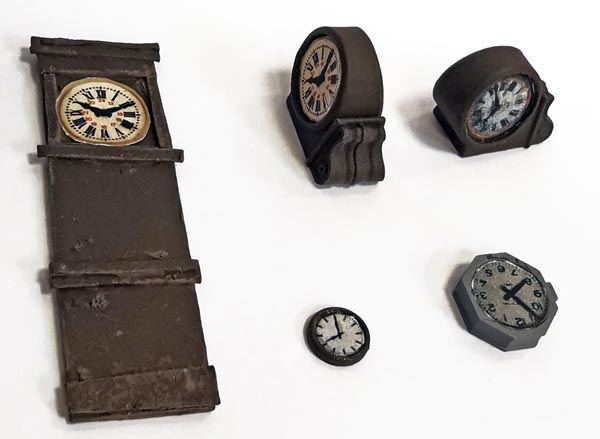 à droite : parlons chronométrie. Pour la façade de sa gare de 3ème classe PLM, Pierre a acquis deux pendules FAB 432 (en haut à droite). Les cadrans sont proposés par COPIRAL en film autocollant. C’est d’ailleurs ce qui a servi à construire celle de gauche (en carton) qui est l’horloge mère à l’intérieur du BV. Cela rappelle à Pierre son début de carrière ! Deux autres pendules FAB 432 avec cadrans COPIRAIL en bas. de la photo.